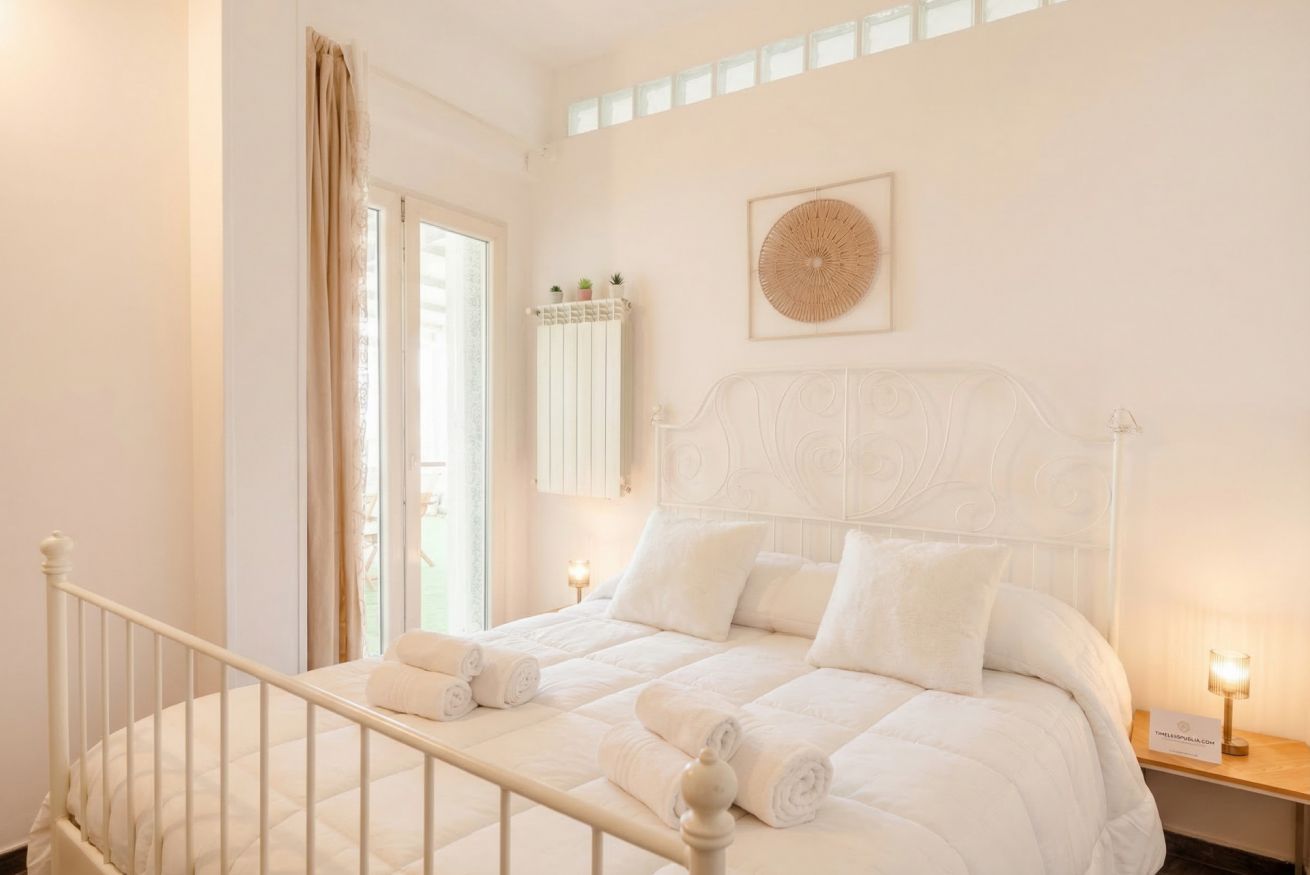 A bedroom with a bed, a window, a wall-mounted shelf with plants, and a decorative wall piece.