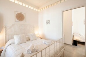 A bedroom with a bed, pillows, a bedside table, a wall clock, and a door. - CarmenLeo-Central Accommodation with Patio (Polignano a Mare)