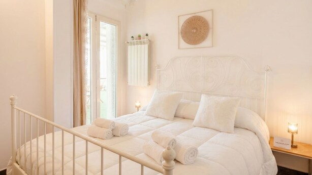 A bedroom with a bed, a window, a wall-mounted shelf with plants, and a decorative wall piece.