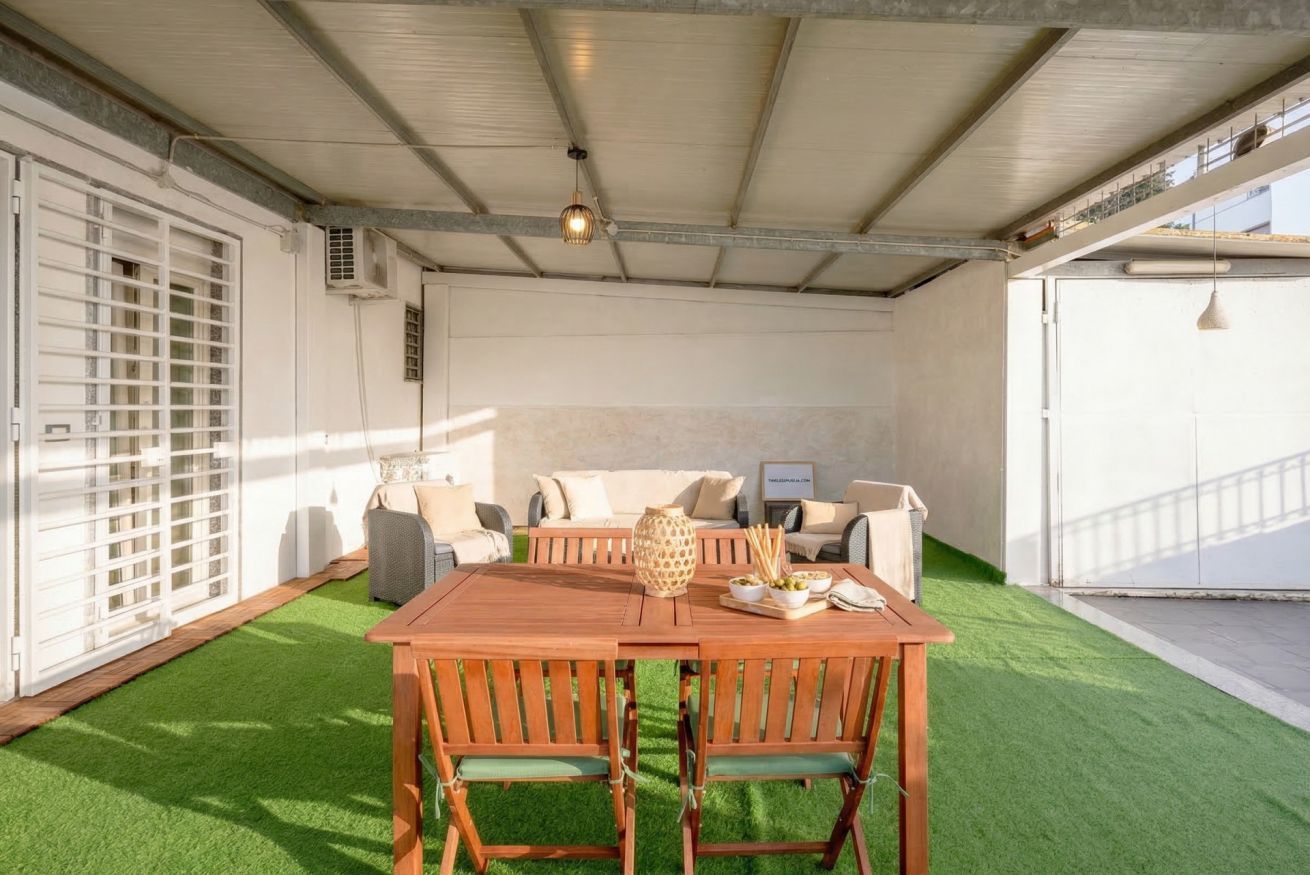 Un espace extérieur abrité, comprenant une table et des chaises en bois, un canapé et un vase décoratif.