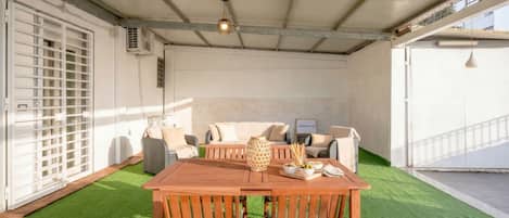 Un espace extérieur abrité, comprenant une table et des chaises en bois, un canapé et un vase décoratif.