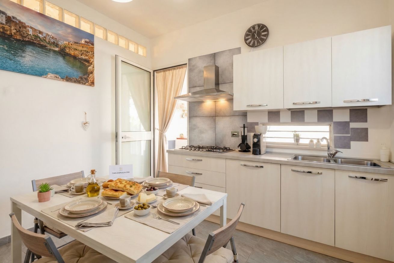 Une cuisine moderne avec une table à manger dressée pour le repas, une cuisinière à gaz et une horloge au mur.