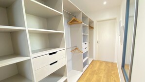 Un dressing accessible sans porte, doté d’étagères ouvertes, d’un portant en bois et d’une porte.