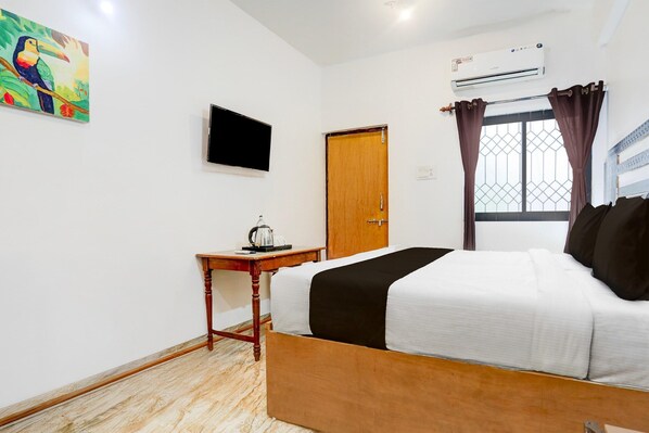 A bedroom with a bed, a television, a wooden door, an air conditioning unit, and a window with curtains.