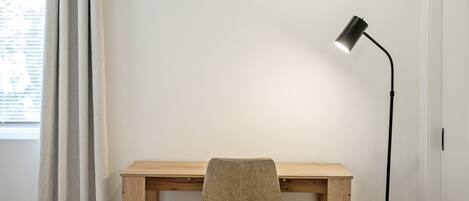 A room with a wooden desk, a chair, a floor lamp, and a window with curtains.