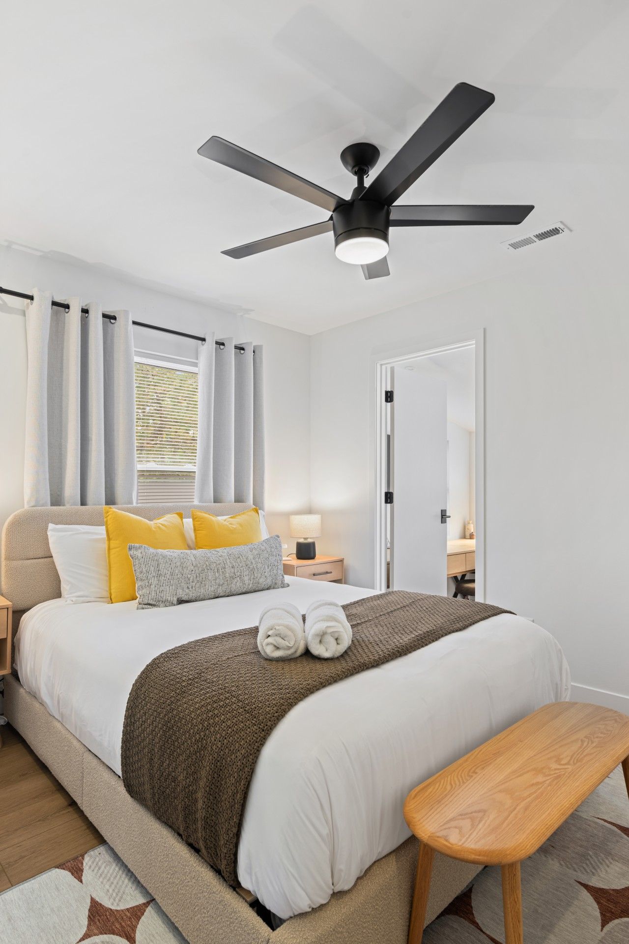 A modern bedroom with a bed, bedside table, lamp, and a ceiling fan.