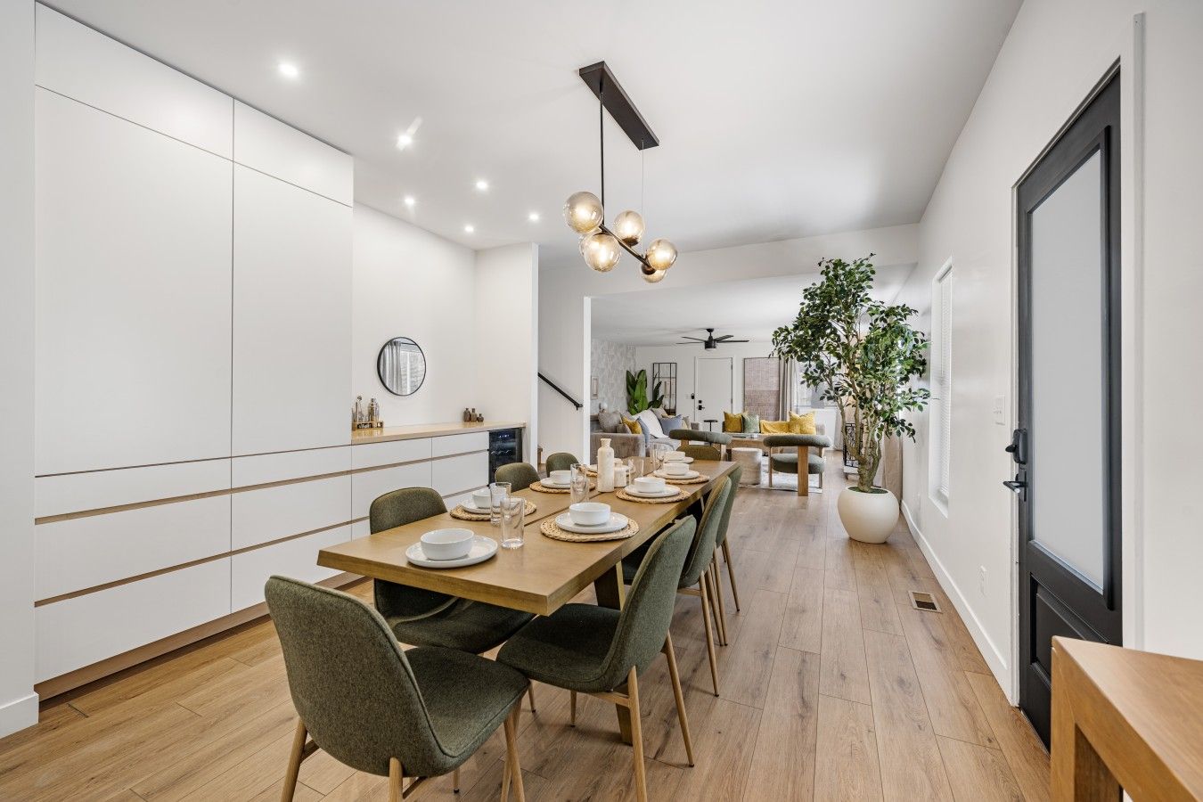A modern dining area with a long table set for a meal, a ceiling fan, and a potted plant.