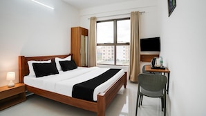 Ein Hotelzimmer mit Bett, Schreibtisch, Stuhl, Fernseher, Kleiderschrank und einem Fenster mit Vorhängen.