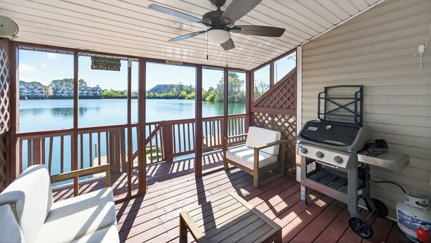 Een overdekt terras met een barbecue, een witte stoel en uitzicht op een meer.