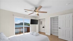 Een slaapkamer met een bed, een plafondventilator, een televisie, een schuifdeur naar een balkon en een witte garderobe.