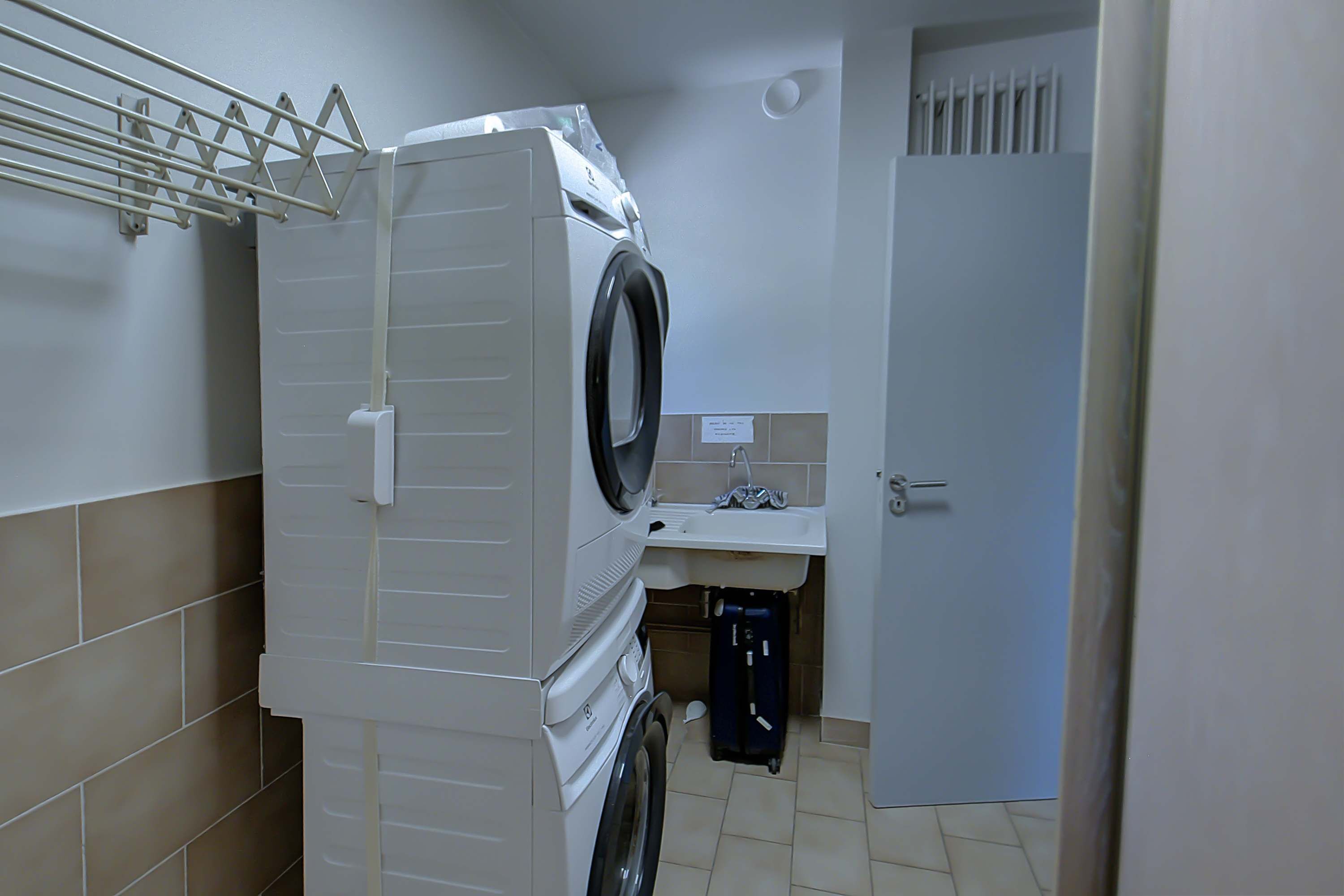 Un espace réduit dédié à la buanderie, comprenant un lave-linge, un étendoir, un évier et une porte.