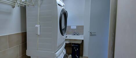 Un espace réduit dédié à la buanderie, comprenant un lave-linge, un étendoir, un évier et une porte.