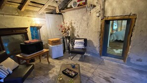 A rustic room with a wooden ceiling, a bench, a table with drinks, and a television.