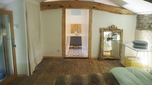 A rustic room with exposed wooden beams, a mirror, a small table, and a view into another room with a window.