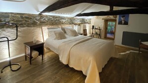 A bedroom with a bed, wooden floor, stone wall, and a sloped ceiling.
