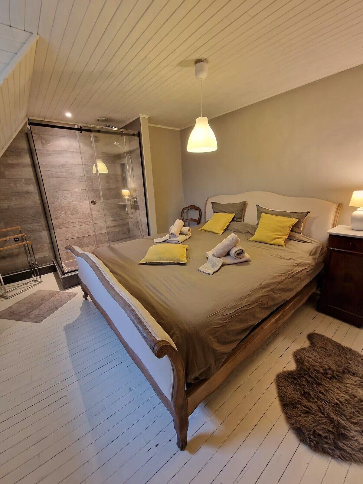Ein Schlafzimmer mit einem großen Bett, einer Duschkabine aus Glas, Holzboden und einer Decke mit Holzbalken.