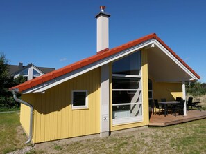 En gul bygning med rødt tag, skorsten og et stort vindue.