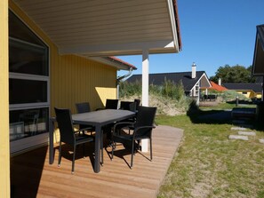 En terrasse med et bord og stole, en træterrasse, og en gul bygning med et vindue.