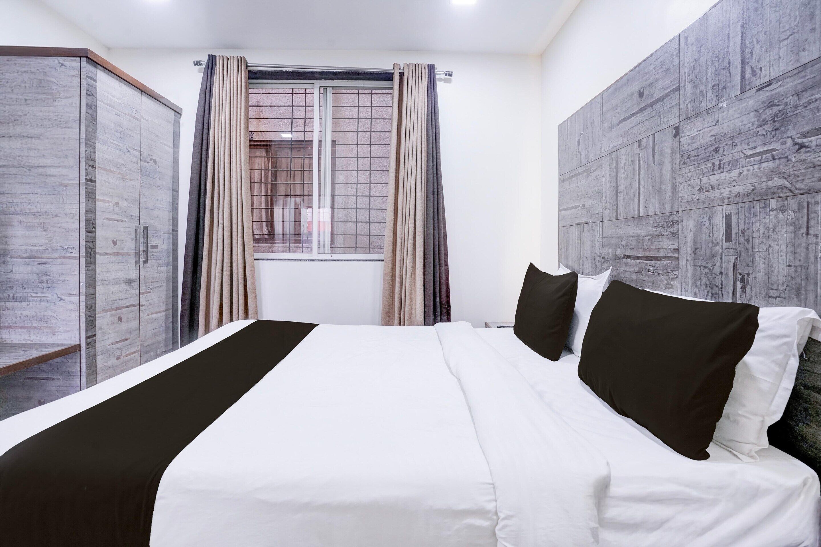 A hotel room with a bed, a wardrobe, a window with curtains, and a wall with a textured design.