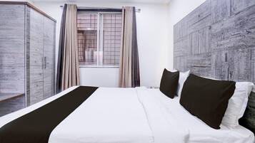 A hotel room with a bed, a wardrobe, a window with curtains, and a wall with a textured design.