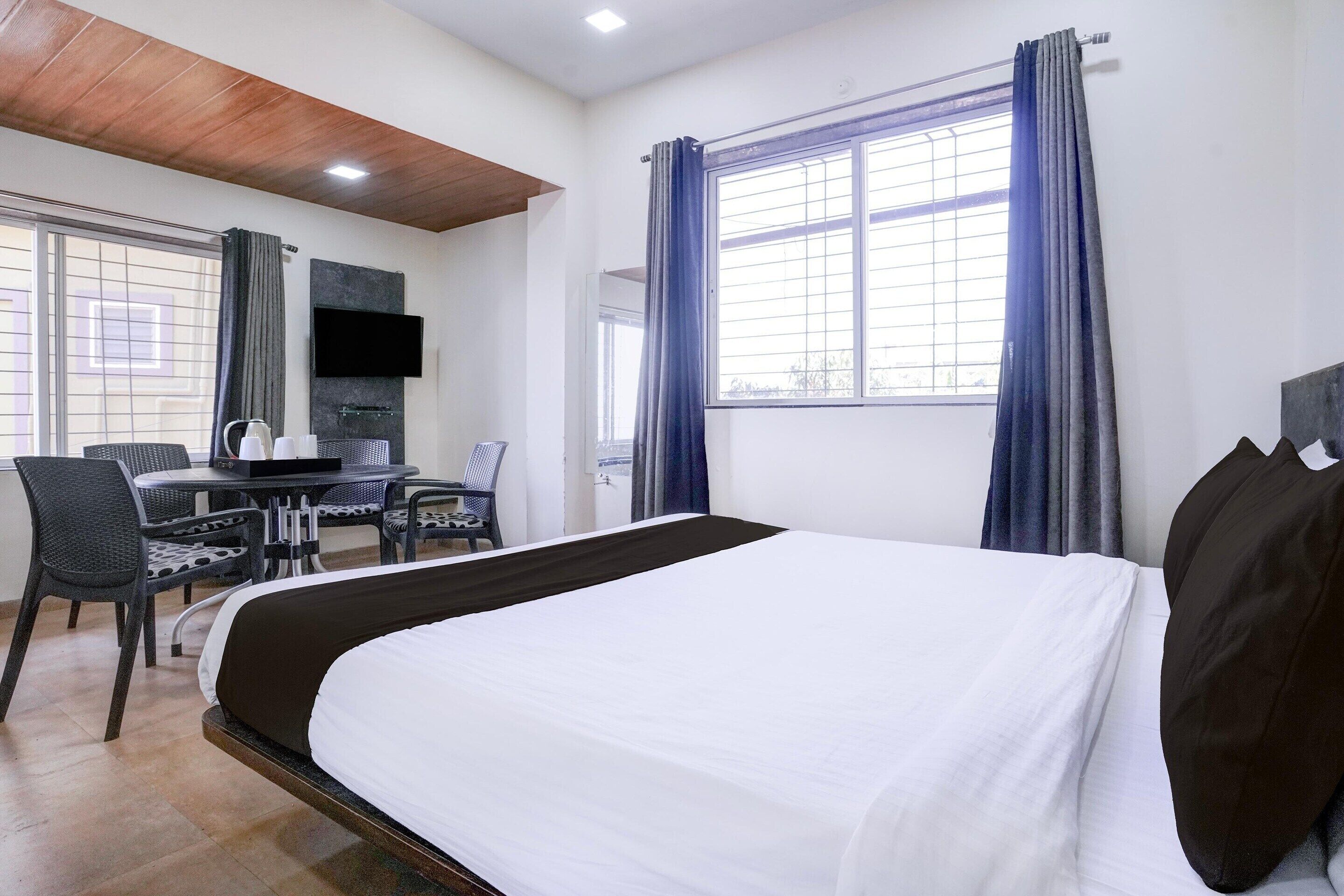 Una habitación de hotel con una cama, un escritorio con silla, televisión y una ventana con cortinas.