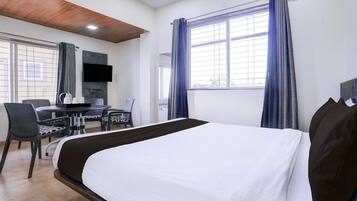 Una habitación de hotel con una cama, un escritorio con silla, televisión y una ventana con cortinas.