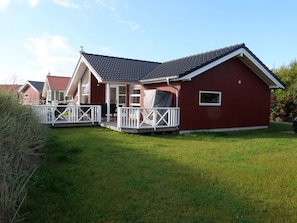 A red building with a covered porch and white railings, surrounded by green grass. - Baltic Coast Home With Private Spa (Grossenbrode)