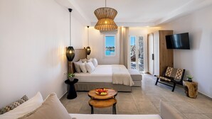 Une chambre d’hôtel moderne, équipée d’un lit, d’une table à manger avec des fruits, d’un canapé, d’une télévision et d’une grande fenêtre donnant sur un beau paysage.