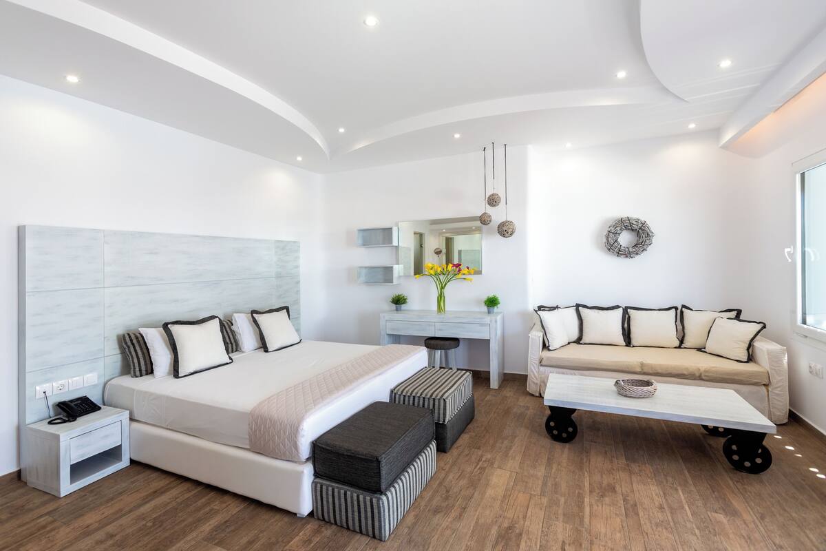 A modern hotel room with a bed, desk, sofa, and a large window.