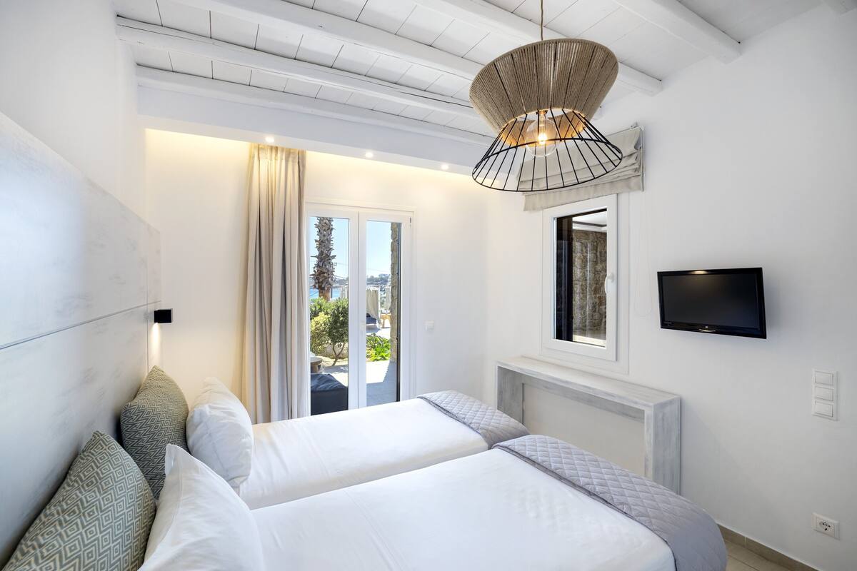 A hotel room with two beds, a television, a large window, and a ceiling fan.