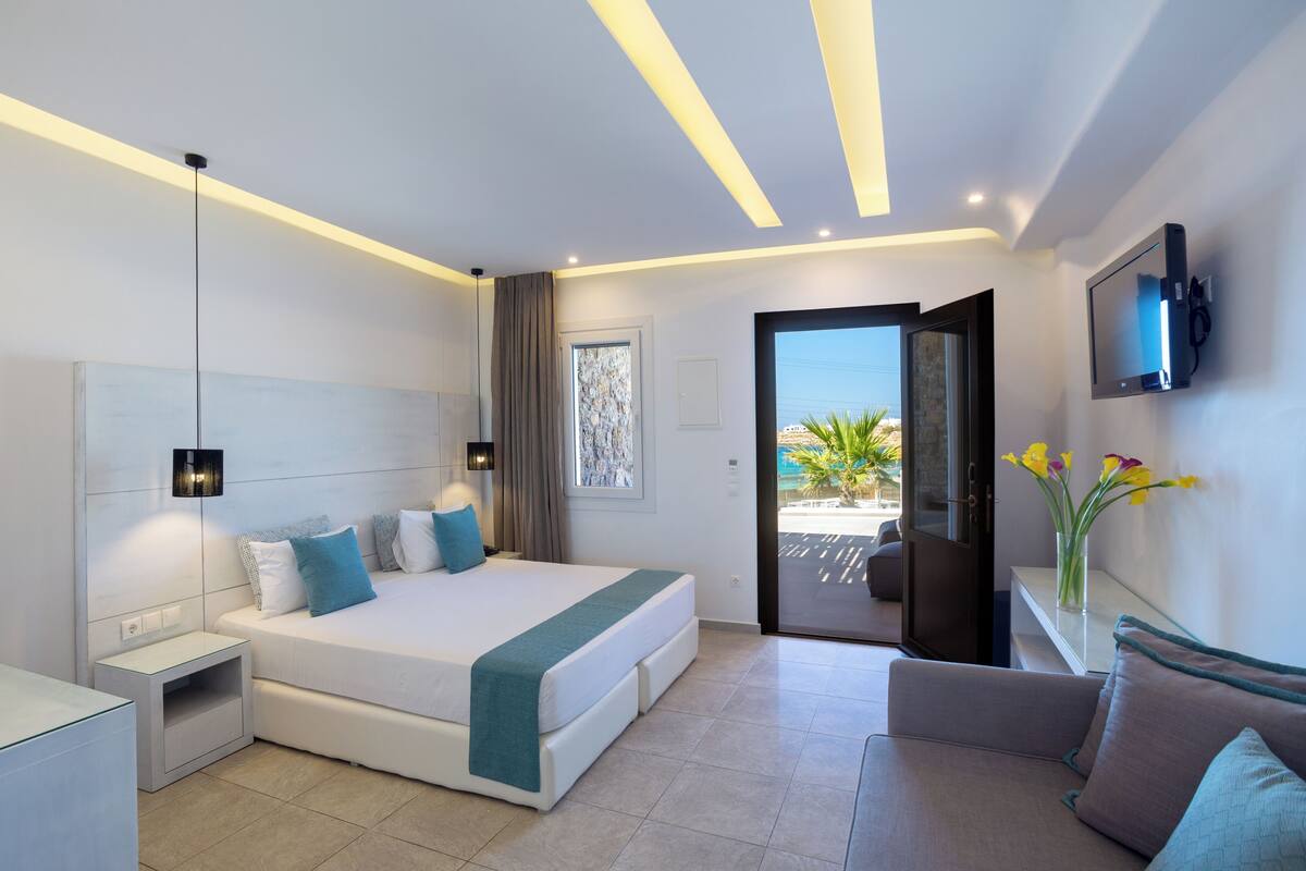 A modern hotel room with a bed, bedside table, TV, and a view of the outdoors.