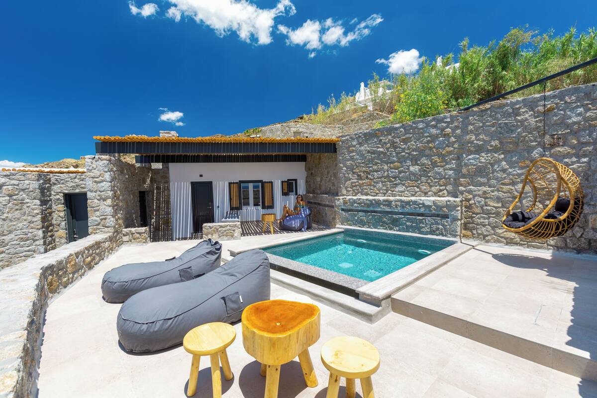 A stone-walled outdoor area with a swimming pool, seating, and a hanging chair.