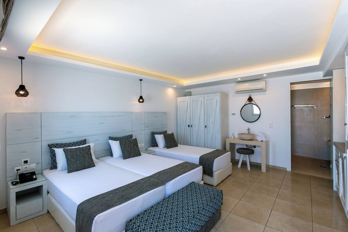A hotel room with two beds, a desk with a mirror, a sink, and a wardrobe.