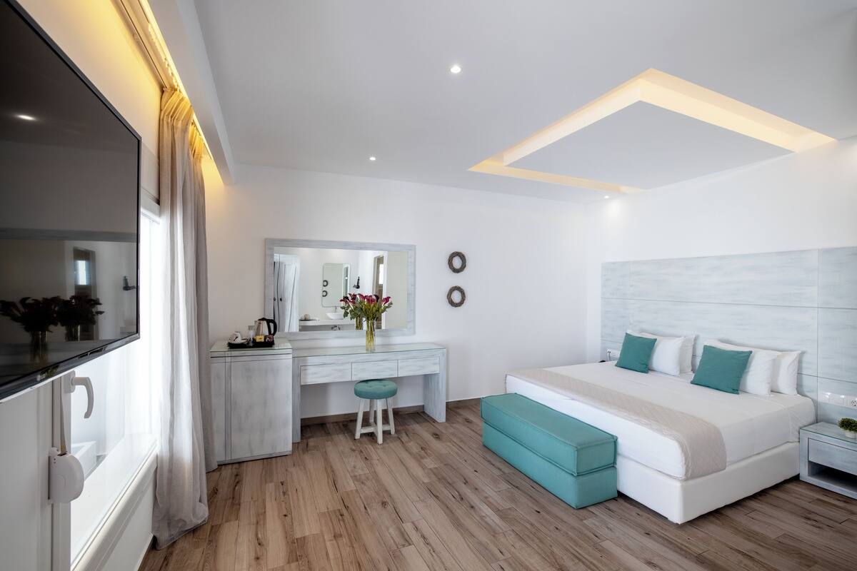 A modern bedroom with a large bed, a desk, a vanity, and a large mirror.