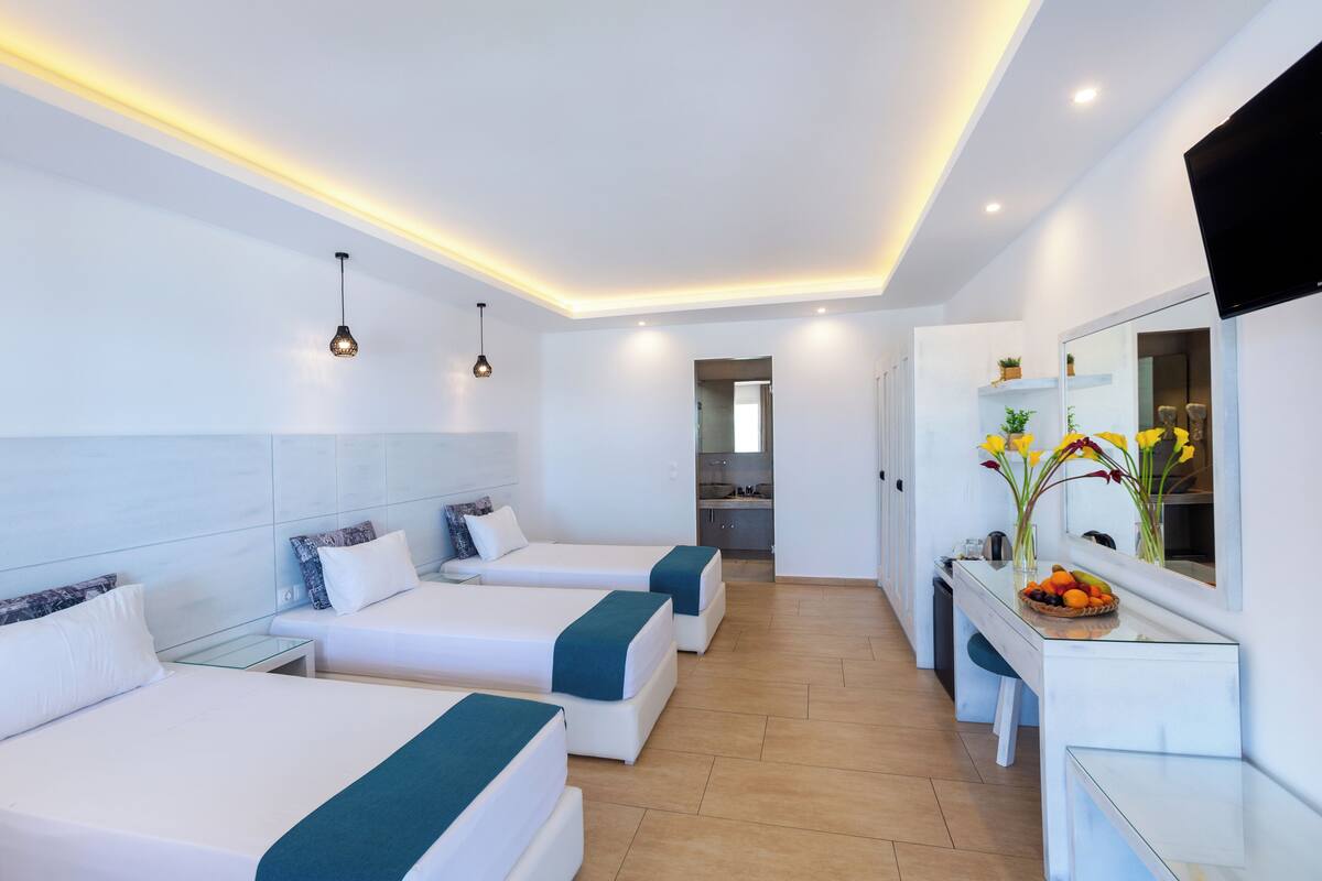 A hotel room with three beds, a small kitchenette, and a bathroom visible through an open door.