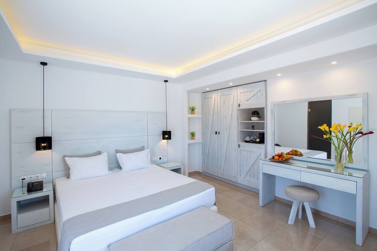 A modern bedroom with a large bed, bedside tables, a desk with a chair, a wardrobe, and a mirror.