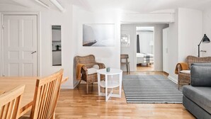 Uma sala de estar moderna com uma mesa de jantar de madeira, cadeiras de vime, um sofá cinza e uma pequena mesa branca.