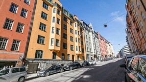 Uma rua com edifícios altos, carros estacionados e céu claro.