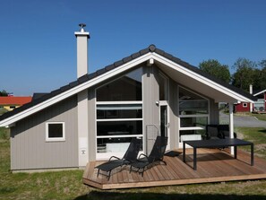 A modern house with a sloped roof, a chimney, and a deck with outdoor furniture. - 4 Star Holiday Home in Grossenbrode (Grossenbrode)