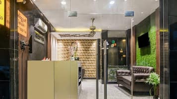 A reception area with a reception desk, a seating area with a sofa, a potted plant, and a wall-mounted TV.
