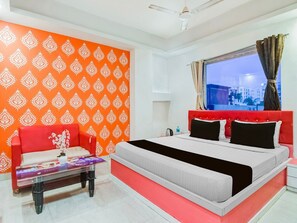 Une chambre d’hôtel avec un lit, un canapé rouge, une petite table avec un vase et une fenêtre avec des rideaux.