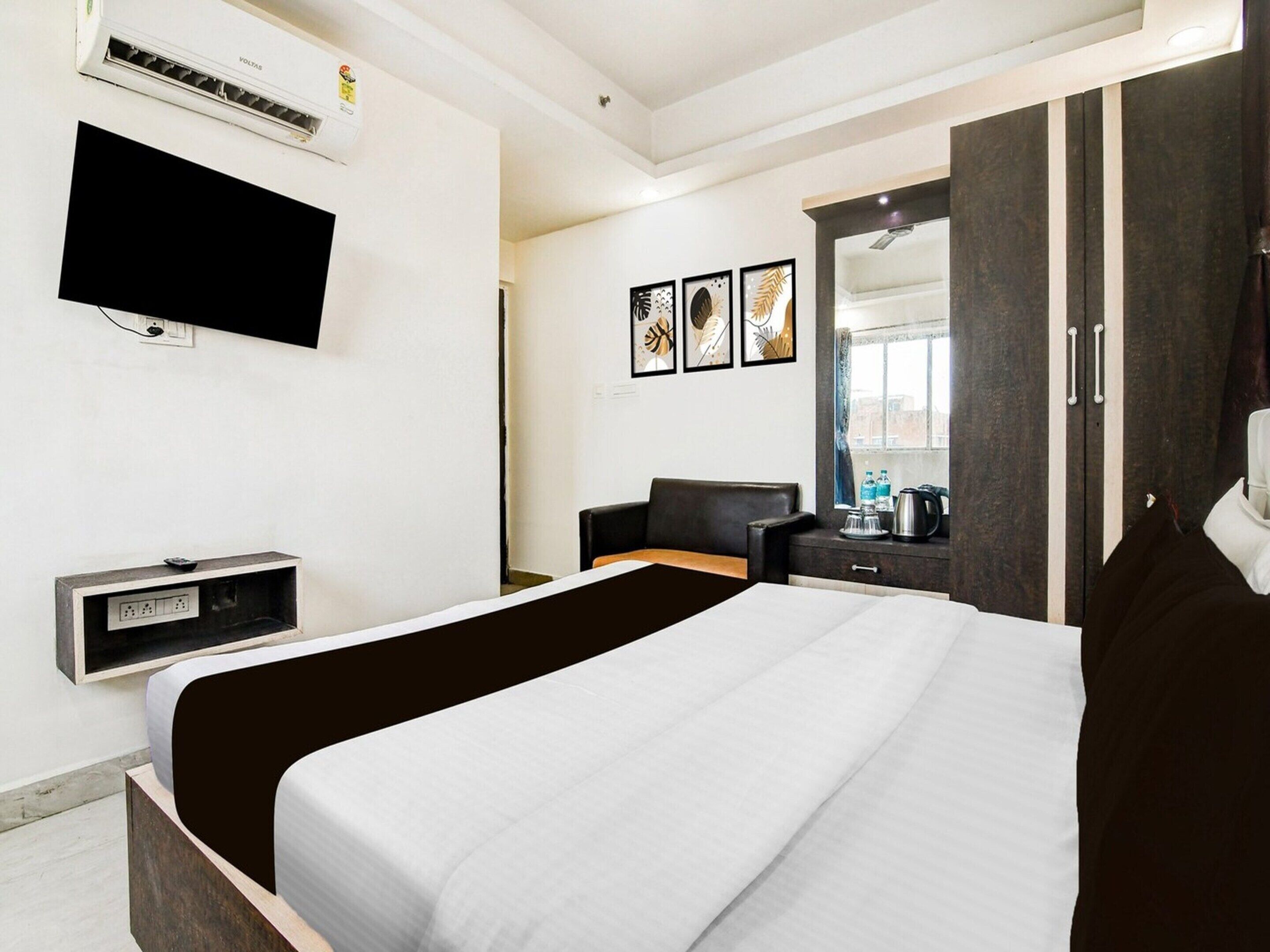 A hotel room with a bed, a TV, a desk, a chair, a wardrobe, and artwork on the wall.