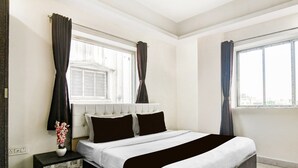 A bedroom with a bed, a nightstand, a window with curtains, and a view of the city. - Classic With Twin Bed Hotel Paradise (Barasat)