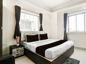 A bedroom with a bed, a nightstand, a window with curtains, and a view of the city. - Classic With Twin Bed Hotel Paradise (Barasat)