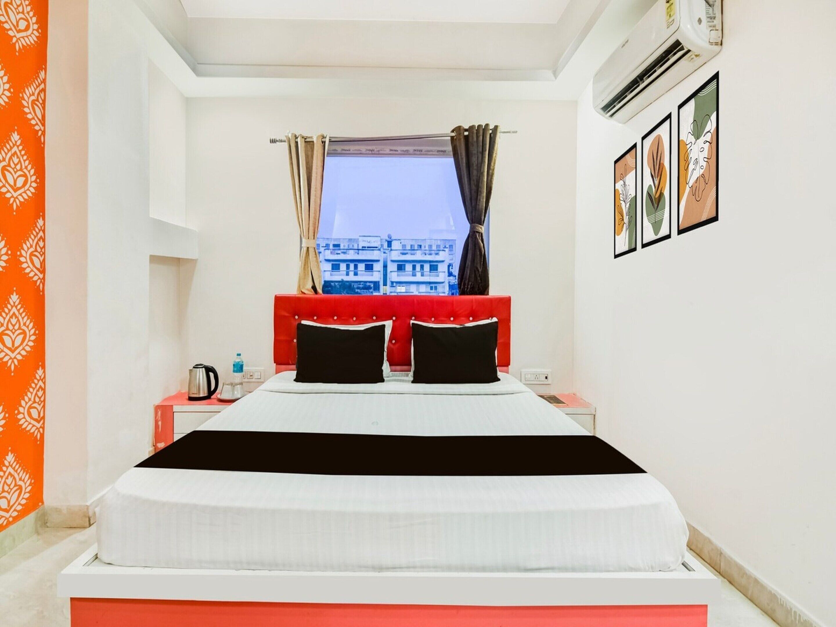 A hotel room with a bed, a window with curtains, an air conditioner, and a wall with framed pictures.