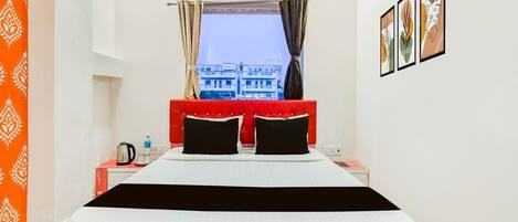 A hotel room with a bed, a window with curtains, an air conditioner, and a wall with framed pictures.