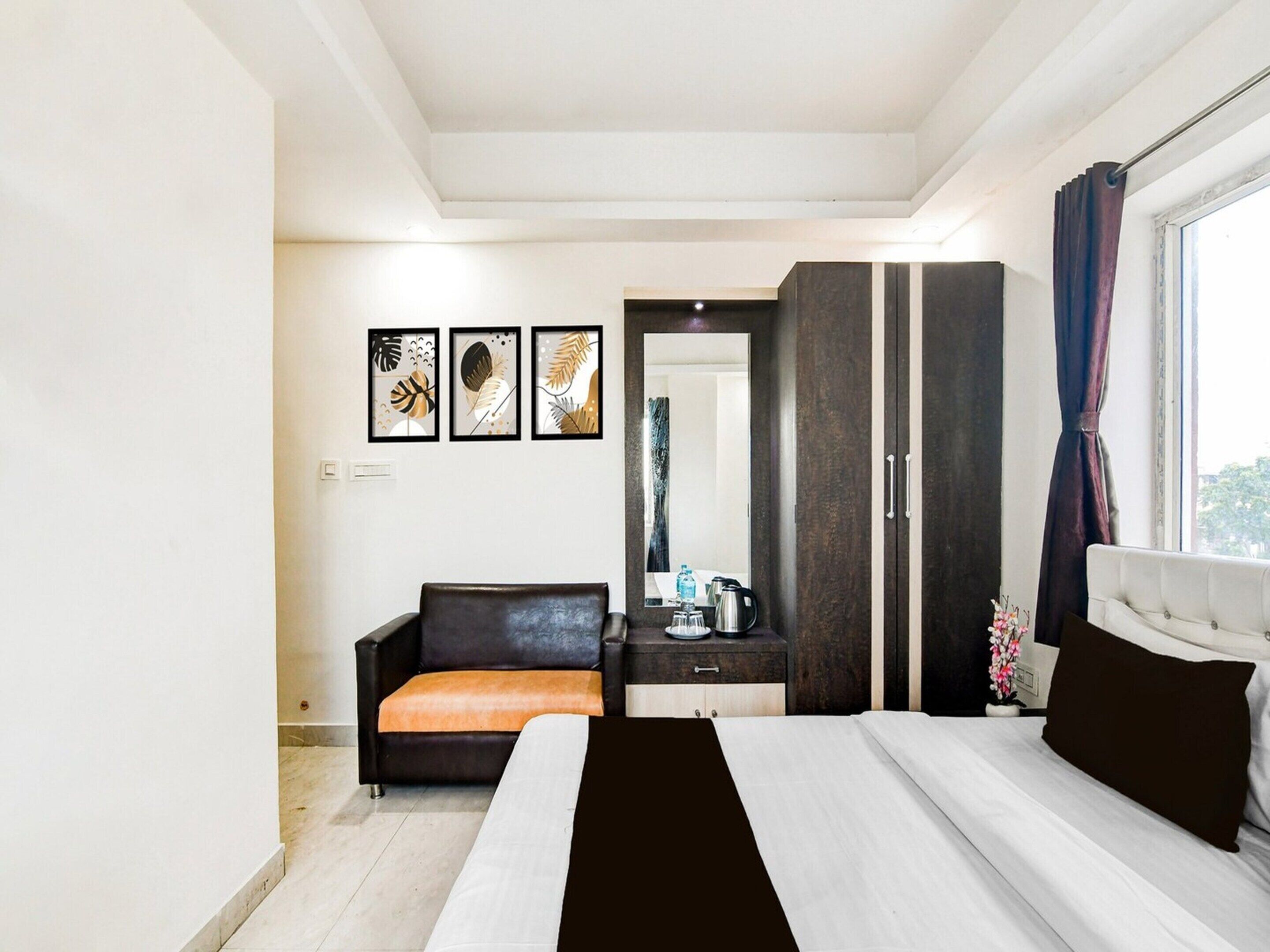 A bedroom with a bed, a sofa, a wardrobe, a mirror, and framed artwork on the wall.