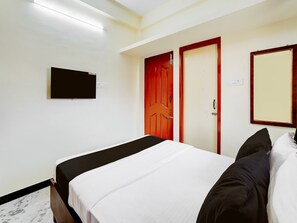 Ein Hotelzimmer mit Bett, Wandfernseher und zwei Türen.