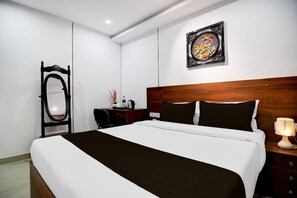 A hotel room with a large bed, a wooden headboard, a bedside table with a lamp, a desk with a chair, and a wall-mounted mirror. - Classic With Twin Bed Victoria Inn (Barasat)