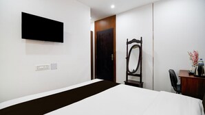 Ein Hotelzimmer mit einem Bett, einem Schreibtisch mit Stuhl, einem an der Wand befestigten Flachbildfernseher und einer Holztür.